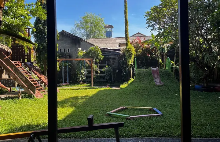 View from a wooden classroom onto a green garden playground