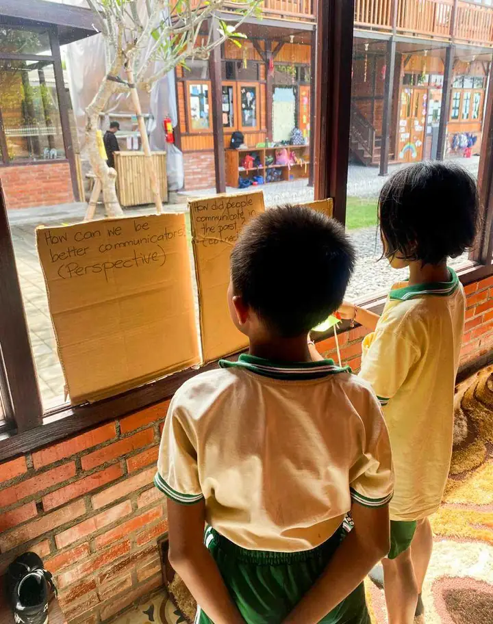 Two students reading inquiry questions written on cardboard at a classroom window