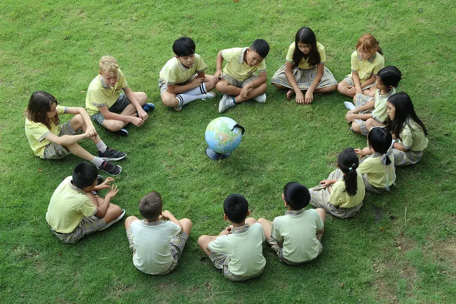 Learners in school uniform sitting in a circle on the grass around a globe